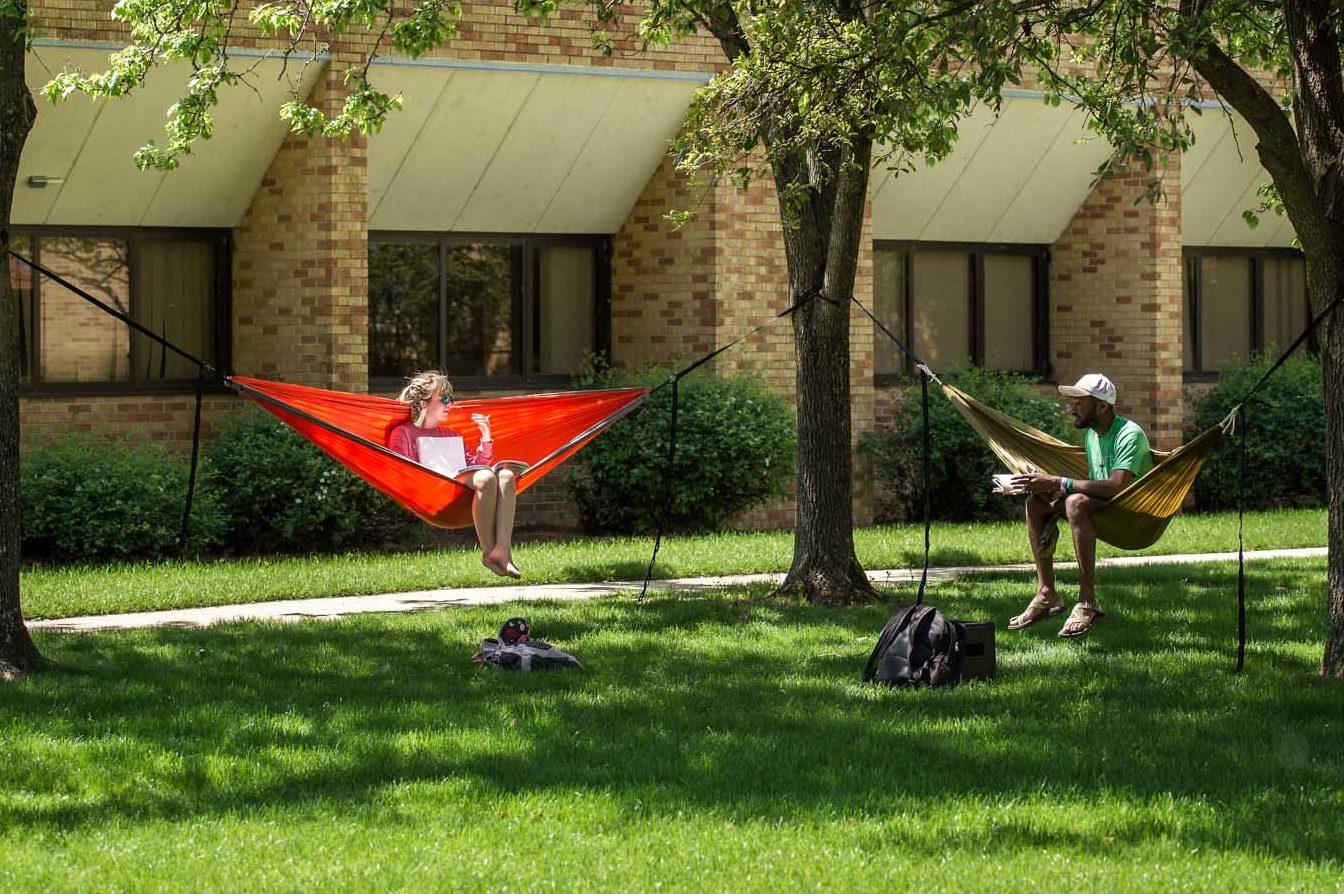 Two students on campus, relaxing in hammocks during summer school.